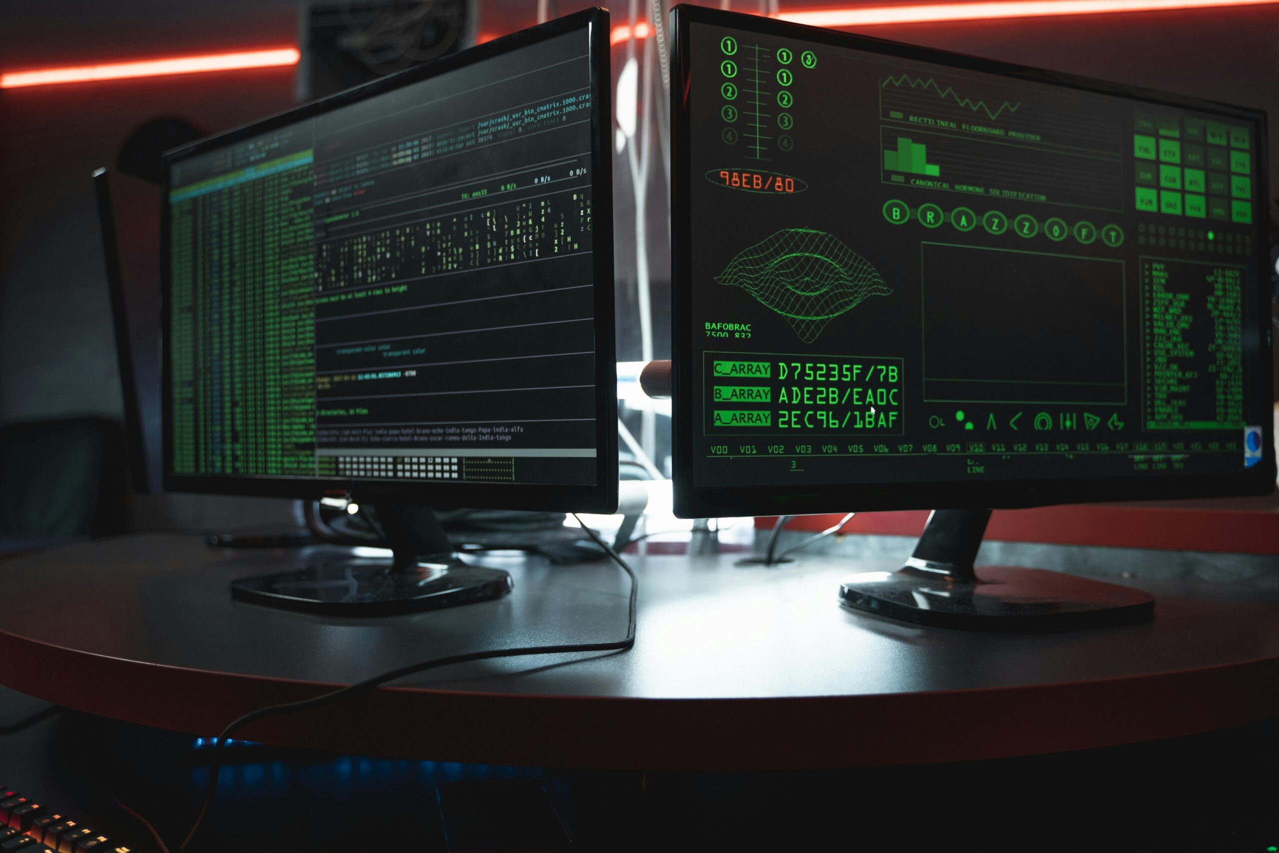 Dijital Davetsiz Misafirler: Virüs, Trojan, Fidye ve Casus Yazılım Nedir? Close-up of dual computer monitors with green coding interfaces in a dark room, highlighting cyber security themes.